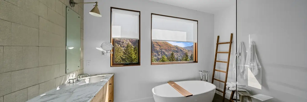 White shades on two windows in a bright bathroom.