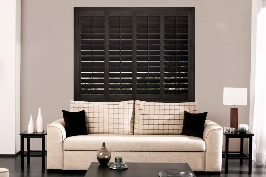 Choose an interior shutter color that coordinates with your room's decor. Dark wood plantation shutters on a window above a beige couch
