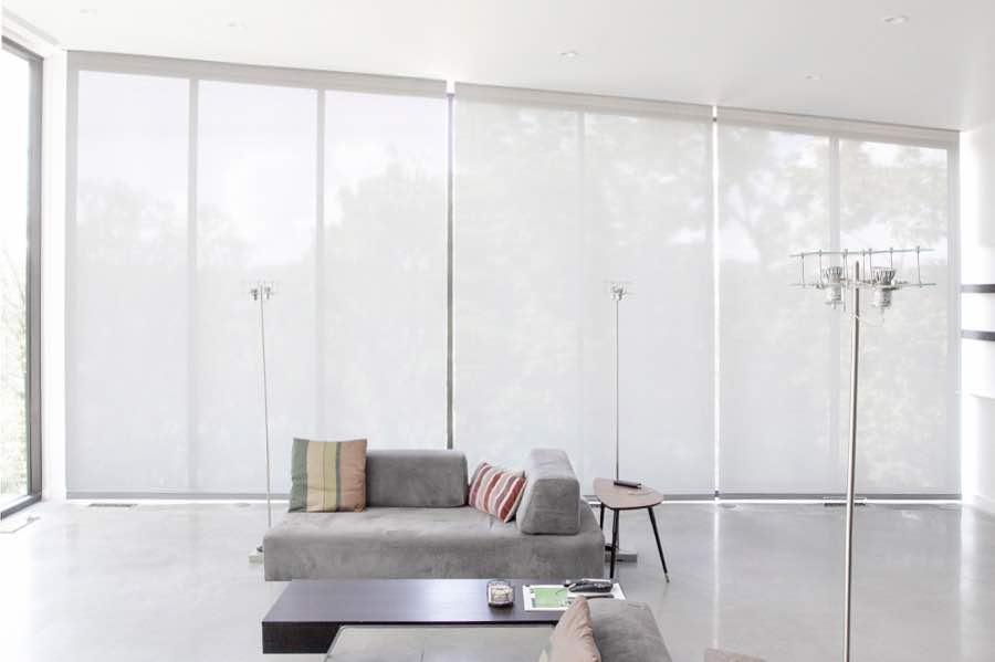 Motorized window shades make controlling natural light effortless in your Charlotte great room. White motorized shades on a wall of tall great room windows