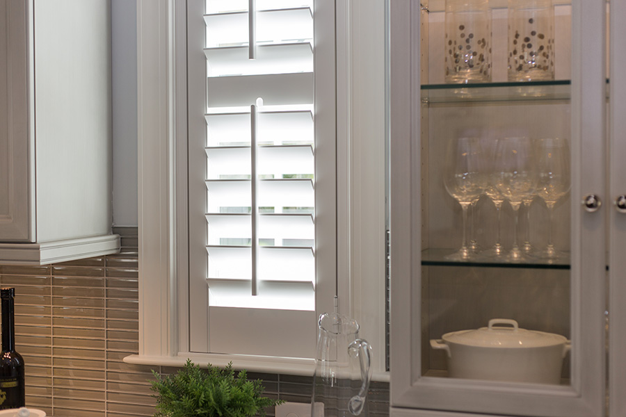 Faux wood Polywood shutters conserve your home's energy all year round. White Polywood shutters above a kitchen sink.