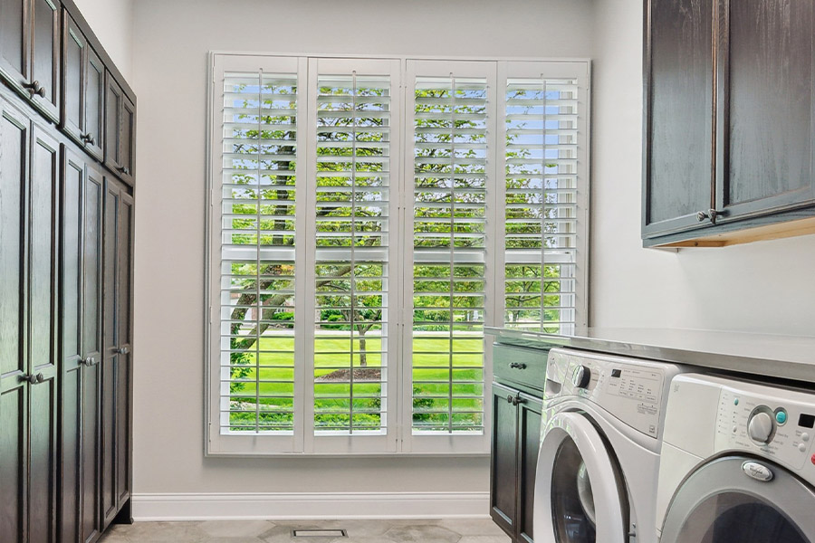 Find the perfect level of natural light for your Charlotte laundry room with interior shutters. White Polywood shutters letting light through a laundry room window