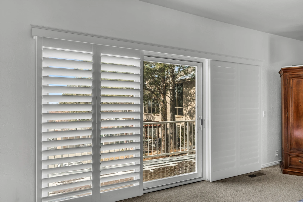 If exceptional light control is a top priority for your sliding door, consider plantation shutters like these. White plantation shutters covering a sliding door in a living room area